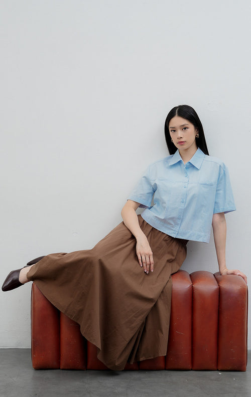 Kemeja kancing depan wanita warna biru muda (light blue) Velira Top berbahan katun terstruktur (structured cotton) dengan detail jahitan bahu (yoke seam detailing) dan lengan pendek.