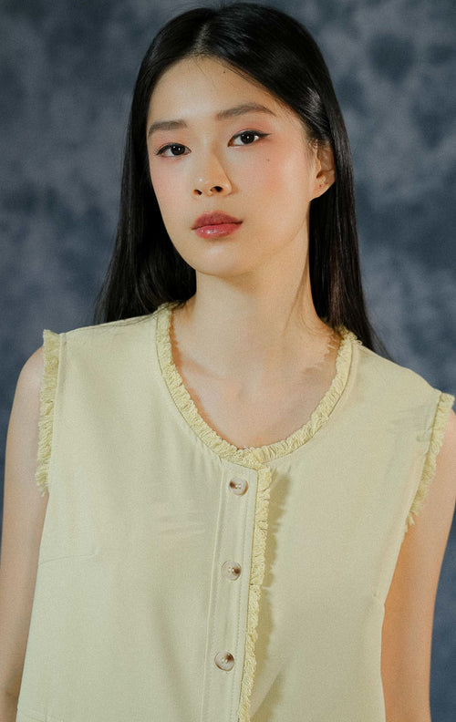 Atasan rompi wanita Venetia warna hijau muda (light green) tanpa lengan seperti pada foto menampilkan detail kancing depan, saku dengan penutup flap, dan aksen fringe/ruffle halus di sepanjang keliman.