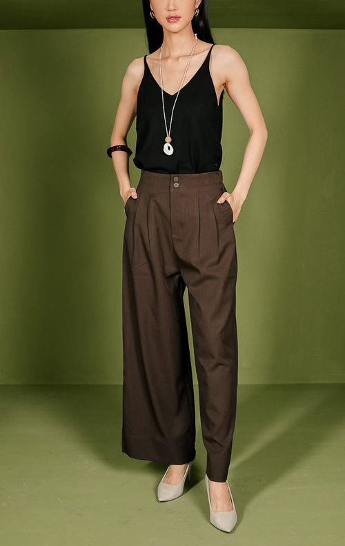 Celana panjang wanita Vincent Pants berpotongan lurus (straight cut) warna cokelat, dilengkapi detail dua kancing bersusun (double button) di ban pinggang depan, aksen lipatan (pleats), saku samping, dan karet elastis di pinggang bagian belakang. 