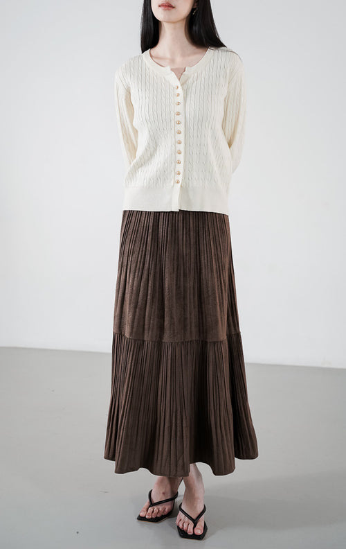 Vinnie Cardigan warna ivory, kardigan rajut kabel (cable knit) lengan panjang dengan detail kancing emas, dipadukan dengan rok plisket cokelat.