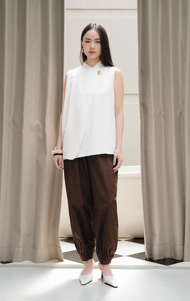 Rompi vest wanita tanpa lengan Viridiana Vest warna ivory krem dengan potongan siluet asimetris wrap berkerah tinggi dan aksen kancing emas elegan.