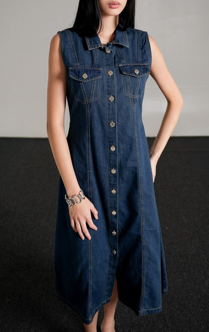 Vivienne Dress Dark Denim, gaun jeans tanpa lengan warna biru tua dengan kerah kemeja dan kancing perak di bagian depan.