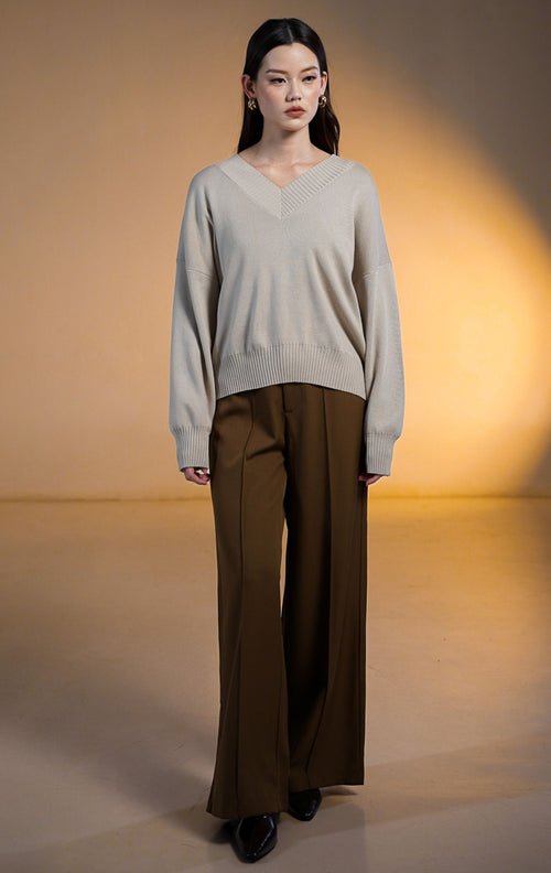 Model wanita memakai Walker Outer Sweater, atasan rajut V-neck warna beige krem dengan celana panjang coklat tua