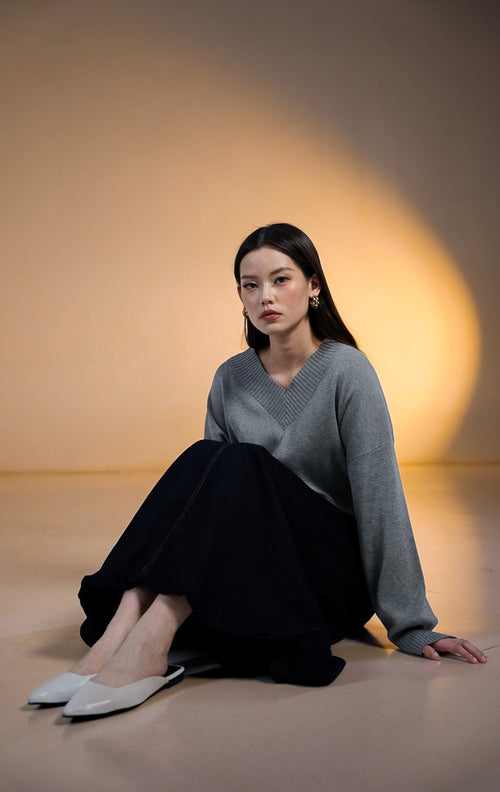 Model wanita memakai Walker Outer Sweater, atasan rajut V-neck warna beige krem dengan celana panjang coklat tua.