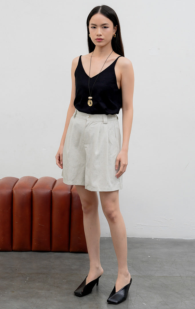 Celana pendek wanita bermuda (Bermuda shorts) warna abu-abu muda (light grey) Walsh Shorts berbahan linen halus dengan aksen lipit (pleats), tempat sabuk, dan kancing depan.