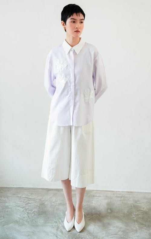 Kemeja wanita lengan panjang motif garis-garis ungu (purple vertical stripes) Wilfred Top dengan detail aplikasi bordir bunga (embroidered floral motifs), kerah dan manset kontras putih (contrasting pointed collar and cuffs), serta bukaan kancing depan. 