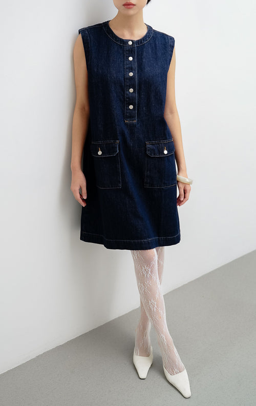 Mini dress wanita tanpa lengan (sleeveless) berbahan denim gelap (dark denim) Winnie Dress dengan kancing jepret (snap-button), saku flap depan, dan saku samping.