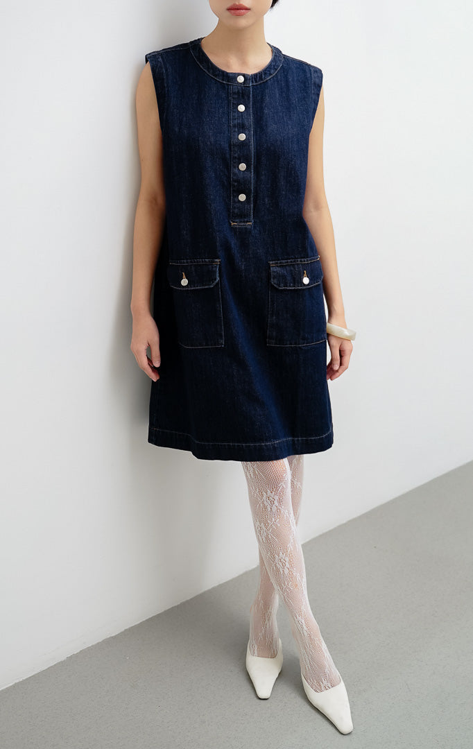 Mini dress wanita tanpa lengan (sleeveless) berbahan denim gelap (dark denim) Winnie Dress dengan kancing jepret (snap-button), saku flap depan, dan saku samping.