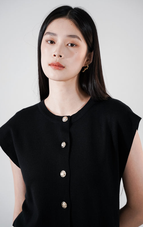 Xandria Set warna hitam, setelan rajut yang terdiri dari atasan tanpa lengan berkancing depan dengan aksen hem warna krem, serta rok panjang hitam senada.

