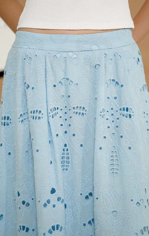 Model berdiri mengenakan Xunera Flowy Broderie Maxi Skirt Light Blue, produk rok panjang wanita model maxi warna biru muda dengan tekstur bordir eyelet lubang-lubang. 