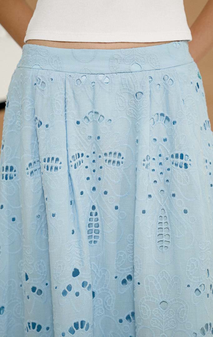 Model berdiri mengenakan Xunera Flowy Broderie Maxi Skirt Light Blue, produk rok panjang wanita model maxi warna biru muda dengan tekstur bordir eyelet lubang-lubang. 