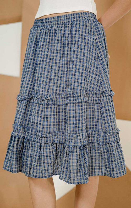 Model berpose mengenakan Yusion Plaid Tier Midi Skirt Navy, produk rok midi wanita motif kotak-kotak dengan model bertingkat dan pinggang karet elastis. 