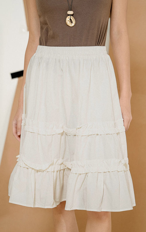 Model berpose dari samping mengenakan Yusion Plaid Tier Midi Skirt White, produk rok midi wanita warna putih dengan model bertingkat dan pinggang karet elastis. 