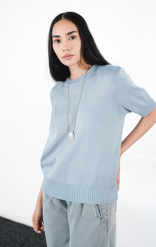 Zaelia Top warna dusty blue, atasan rajut lengan pendek berkerah bulat (crewneck) dengan detail rib, dipadukan dengan kalung liontin perak.