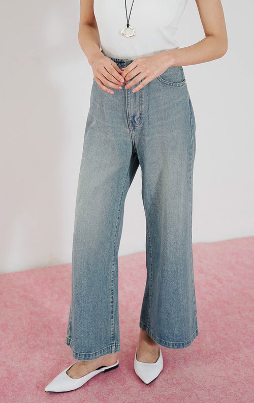 Model wanita mengenakan Zeline High Waist Denim Pants warna biru muda berpotongan lebar dengan detail dua kancing depan, dipadukan dengan tanktop putih.