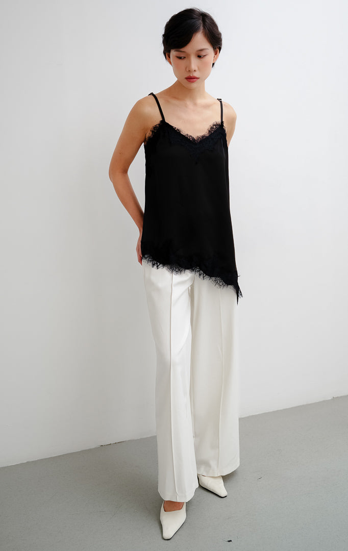 Atasan tank top wanita warna hitam (black) Zilia Top berbahan satin halus dengan renda (lace trim) dan potongan bawah asimetris (asymmetrical hem).