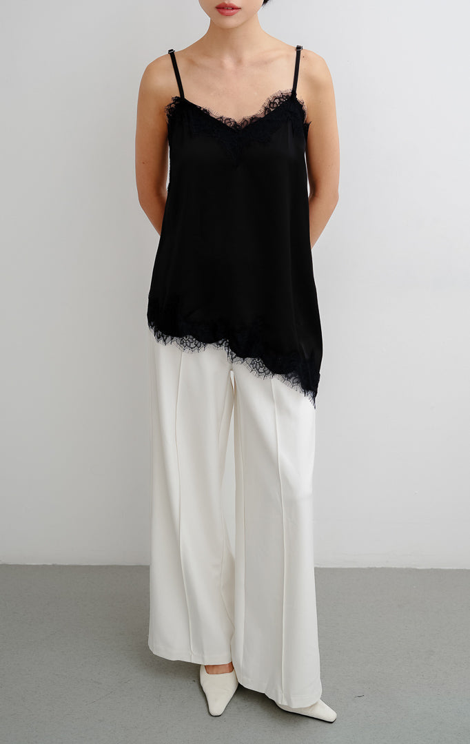 Atasan tank top wanita warna hitam (black) Zilia Top berbahan satin halus dengan renda (lace trim) dan potongan bawah asimetris (asymmetrical hem).