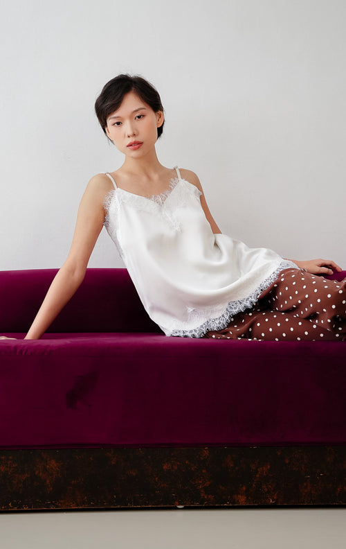 Atasan tank top wanita warna putih (white) Zilia Top berbahan satin halus dengan renda (lace trim) dan potongan bawah asimetris (asymmetrical hem).