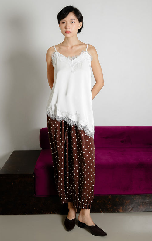 Atasan tank top wanita warna putih (white) Zilia Top berbahan satin halus dengan renda (lace trim) dan potongan bawah asimetris (asymmetrical hem).