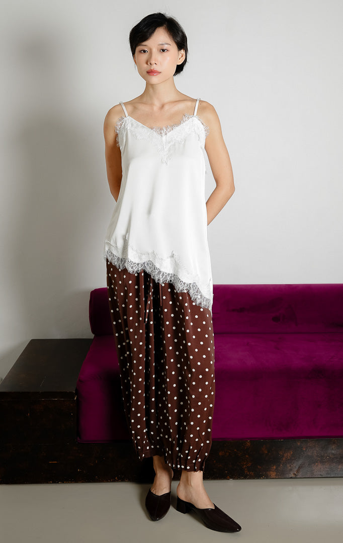 Atasan tank top wanita warna putih (white) Zilia Top berbahan satin halus dengan renda (lace trim) dan potongan bawah asimetris (asymmetrical hem).